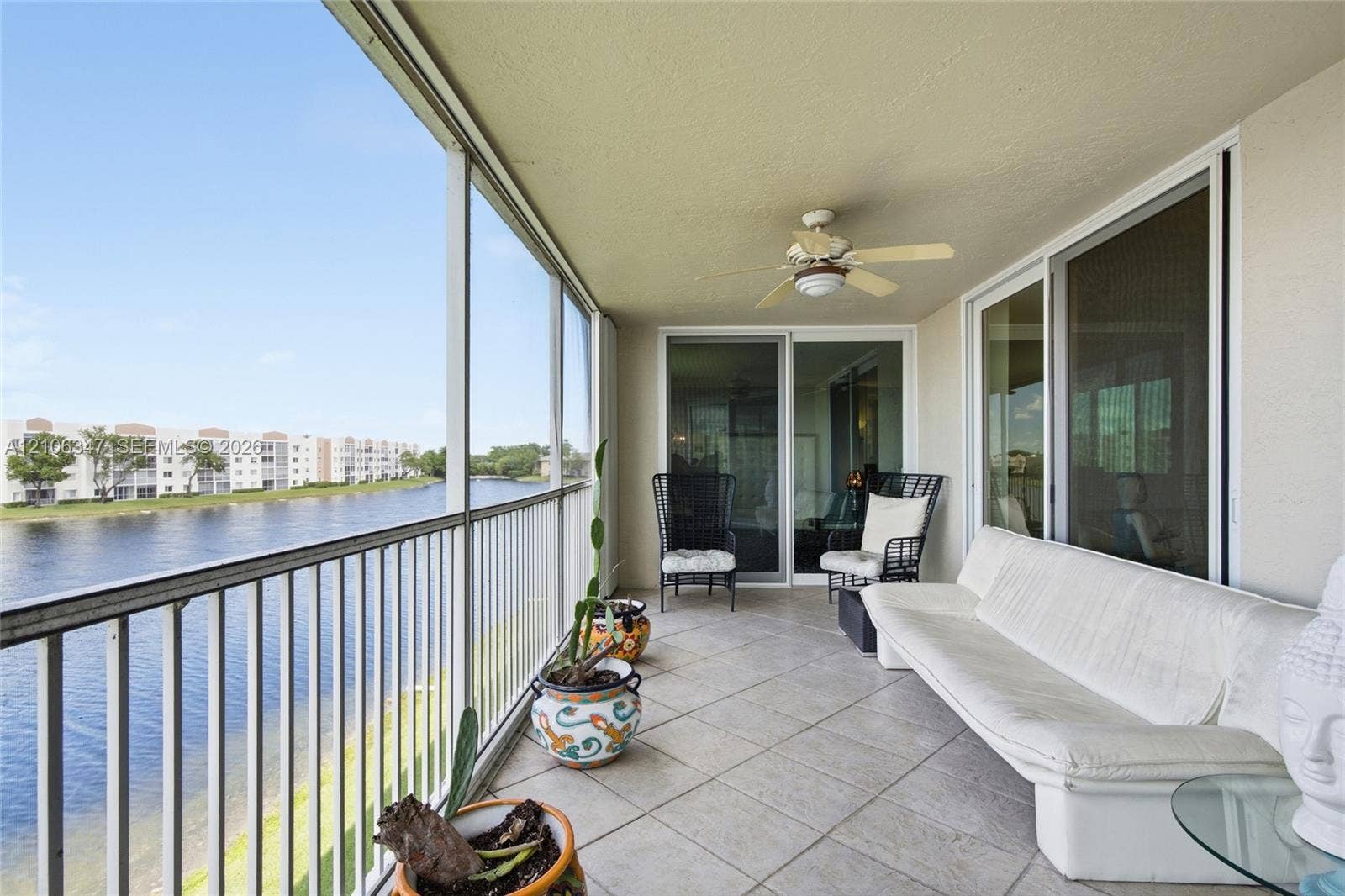 7759 Granville Drive, #306, Tamarac, FL 33321 Screened-in balcony featuring tile flooring, a ceiling fan, and metal railings overlooking a lake