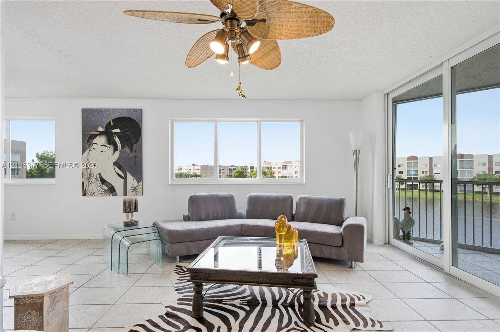 7759 Granville Drive, #306, Tamarac, FL 33321 Living area featuring large format tile flooring, a multi-blade ceiling fan with integrated lighting, oversized picture windows, and sliding glass doors with direct exterior access