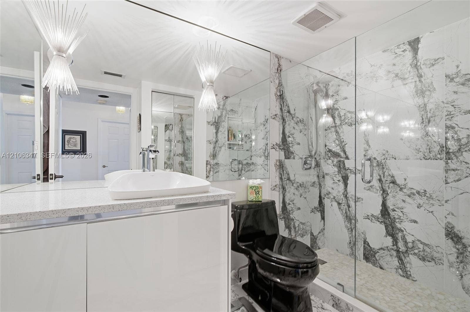 7759 Granville Drive, #306, Tamarac, FL 33321 Bathroom featuring floor-to-ceiling veined stone-style tile shower, frameless glass enclosure, glossy white vanity with integrated basin, expansive wall mirror, and dual starburst-style wall-mounted lighting
