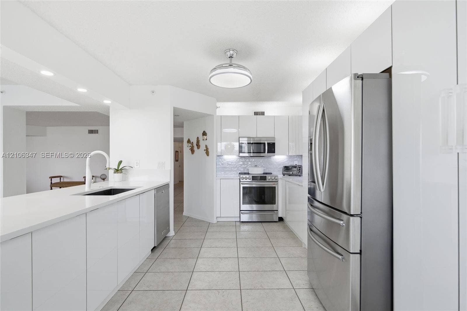 7759 Granville Drive, #306, Tamarac, FL 33321 Kitchen featuring glossy white flat-panel cabinetry, stainless steel appliances, white stone countertops, tile flooring, and a modern gooseneck faucet