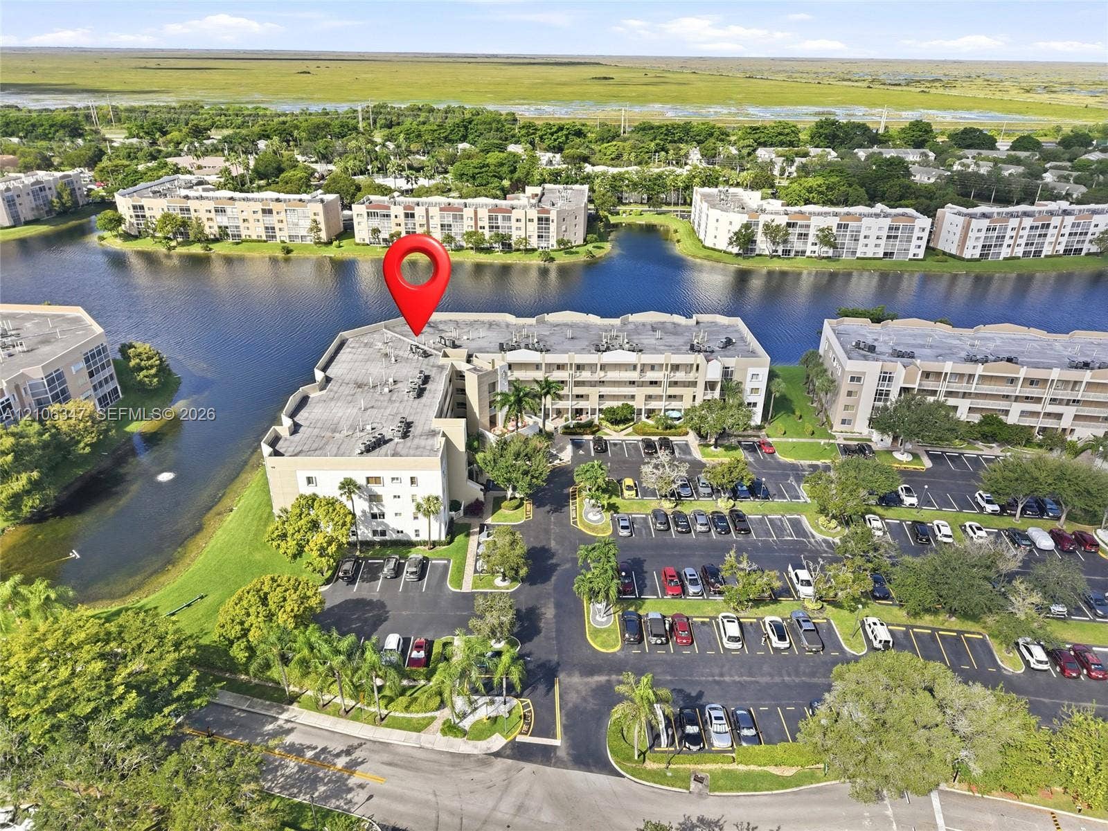 7759 Granville Drive, #306, Tamarac, FL 33321 Multi-story residential building featuring asphalt shingle roofing, paved parking lot, waterfront positioning, and mature palm trees