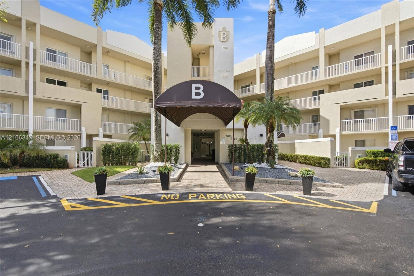 7759 Granville Drive, #306, Tamarac, FL 33321 Multi-story building exterior featuring a covered entryway with awning, integrated balconies, paver stone hardscaping, and mature palm landscaping
