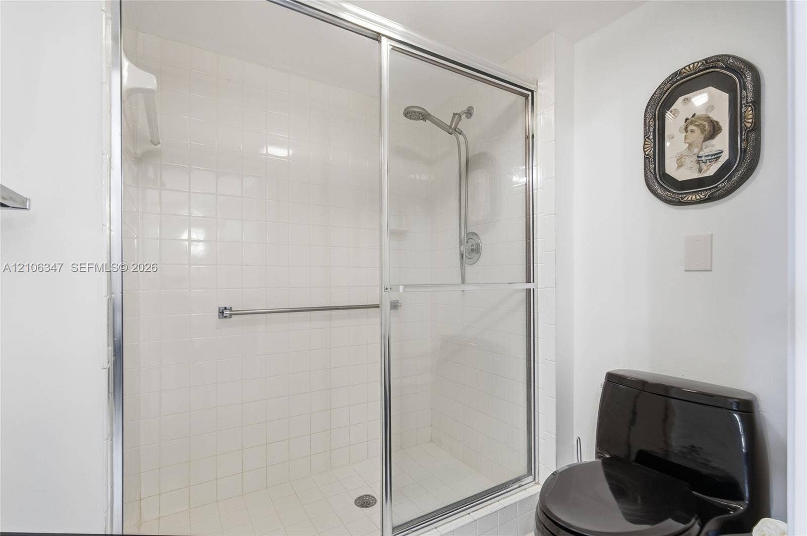 7759 Granville Drive, #306, Tamarac, FL 33321 Walk-in shower enclosure with white tiled surround, chrome sliding doors, wall-mounted adjustable shower head, and integrated grab bar