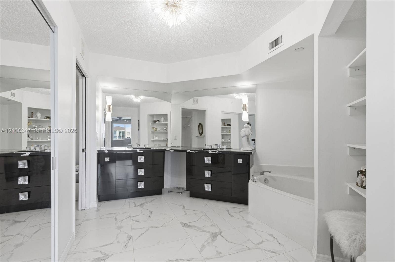 7759 Granville Drive, #306, Tamarac, FL 33321 Large-format white tile flooring with grey veining, dual-basin vanity with dark cabinetry, expansive wall-to-wall mirrors, built-in shelving, and a deep soaking tub
