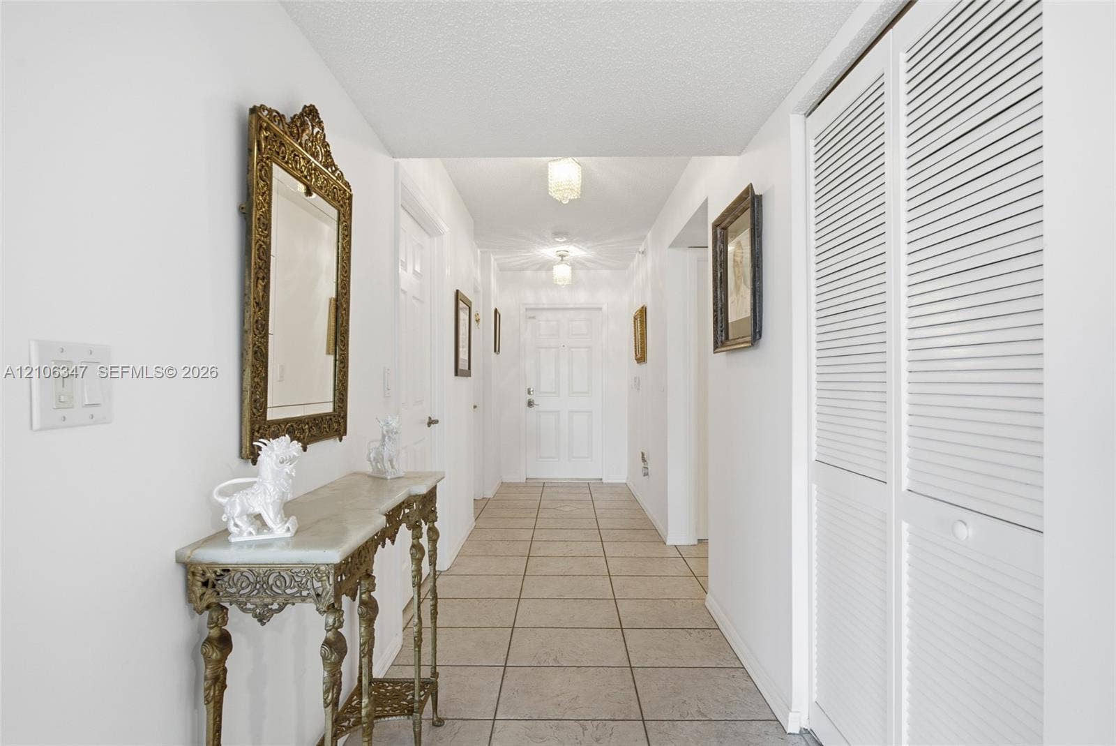 7759 Granville Drive, #306, Tamarac, FL 33321 Interior hallway featuring neutral tile flooring, louvered closet doors, and multiple flush-mount ceiling light fixtures