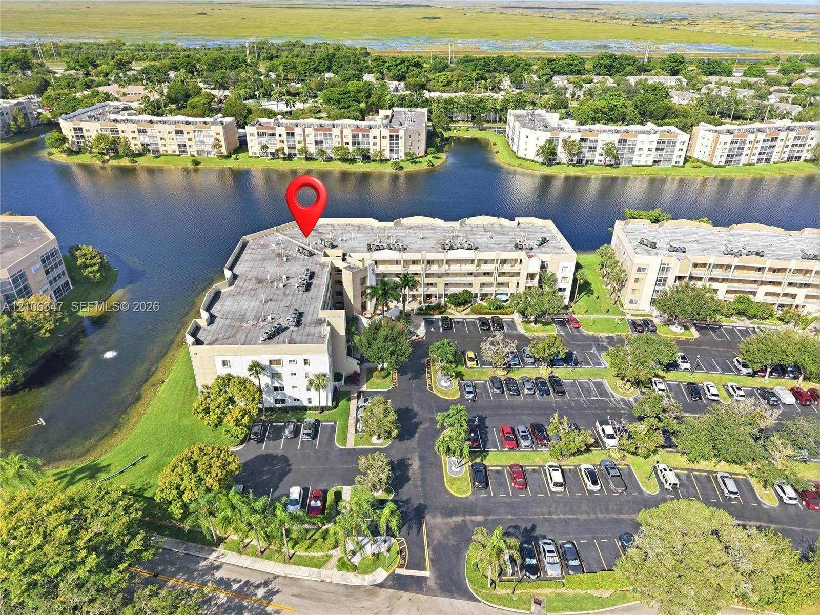 7759 Granville Drive, #306, Tamarac, FL 33321 Aerial perspective of a multi-story residential building featuring waterfront positioning, dedicated surface parking, and manicured landscaping
