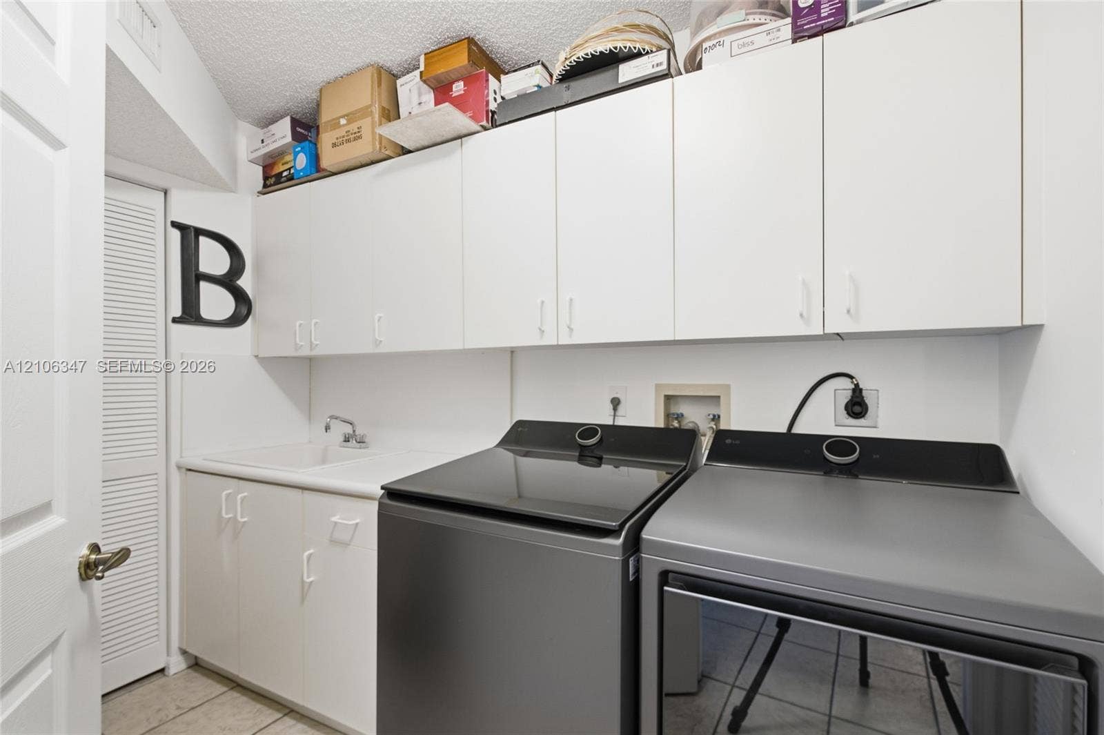 7759 Granville Drive, #306, Tamarac, FL 33321 Laundry space featuring white upper and lower cabinetry, a built-in utility sink with a chrome faucet, and tile flooring