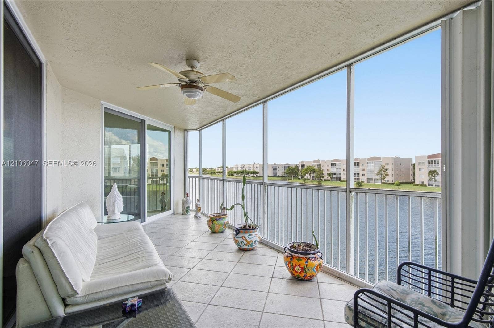 7759 Granville Drive, #306, Tamarac, FL 33321 Screened-in balcony featuring tile flooring, a ceiling fan, and metal railings overlooking a lake
