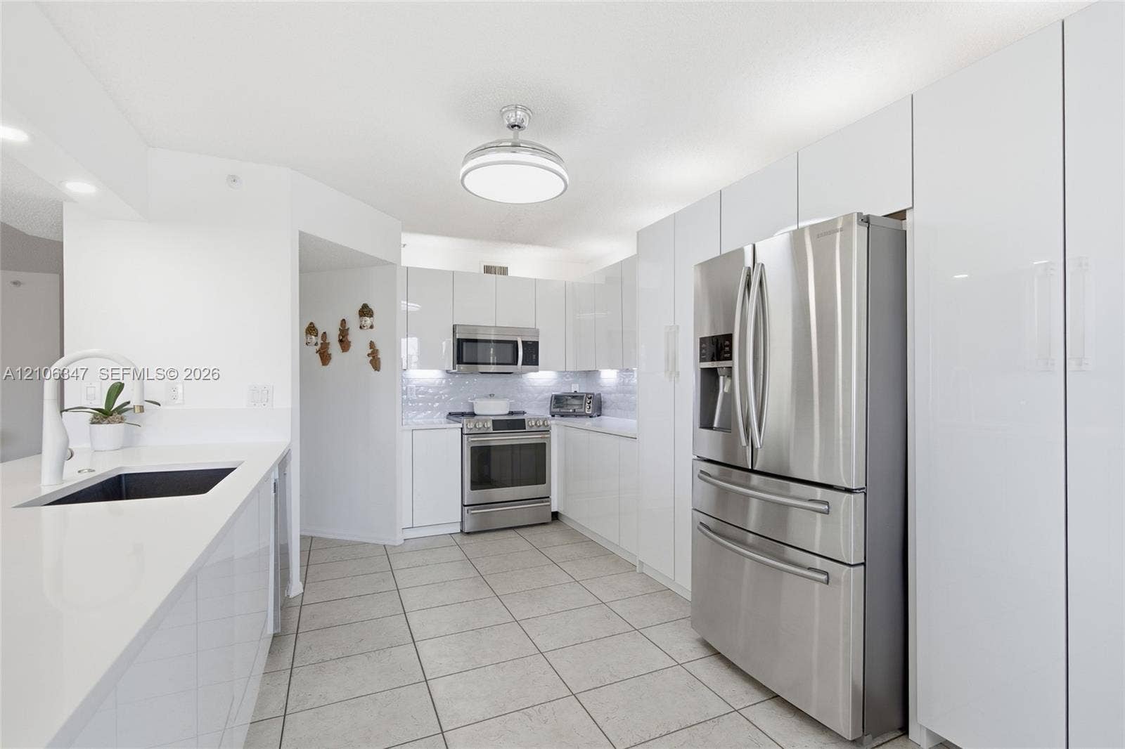 7759 Granville Drive, #306, Tamarac, FL 33321 Kitchen featuring high-gloss white cabinetry, stainless steel appliances, white solid-surface countertops, tile flooring, and a flush-mount ceiling fixture
