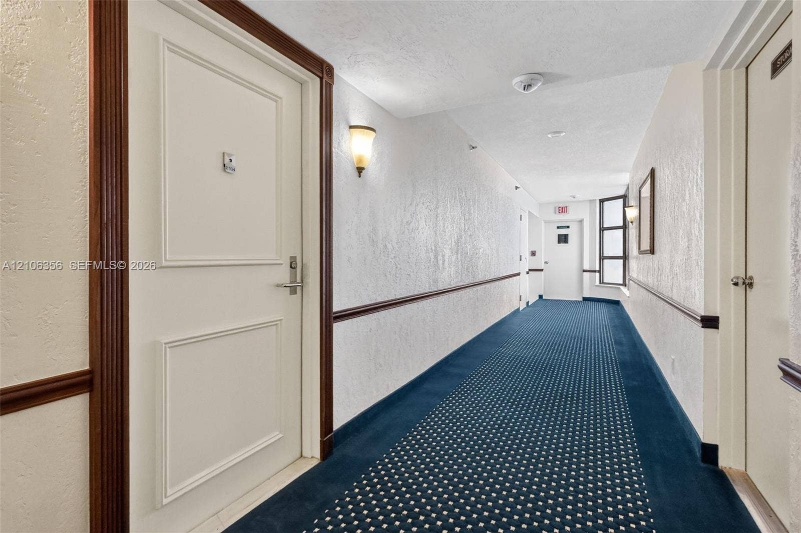 Hallway featuring patterned carpeting, paneled interior doors, wood-finish door casing and chair rail, and wall-mounted sconce lighting