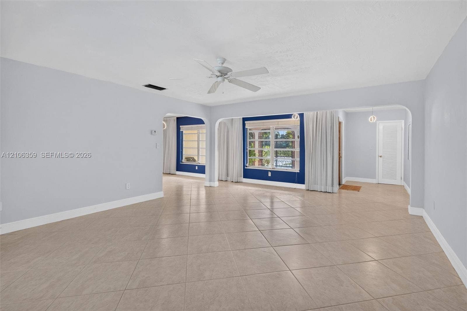 Open interior featuring large-format tile flooring, arched structural openings, a ceiling fan, and multi-pane windows