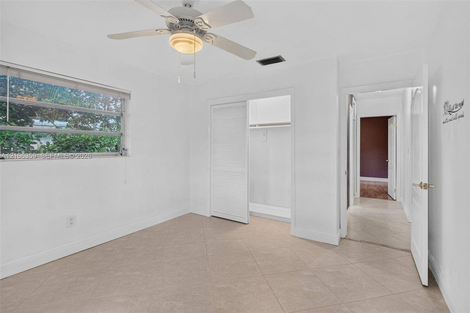 Neutral-toned tile flooring, louvered closet doors, and an overhead ceiling fan with integrated light fixture