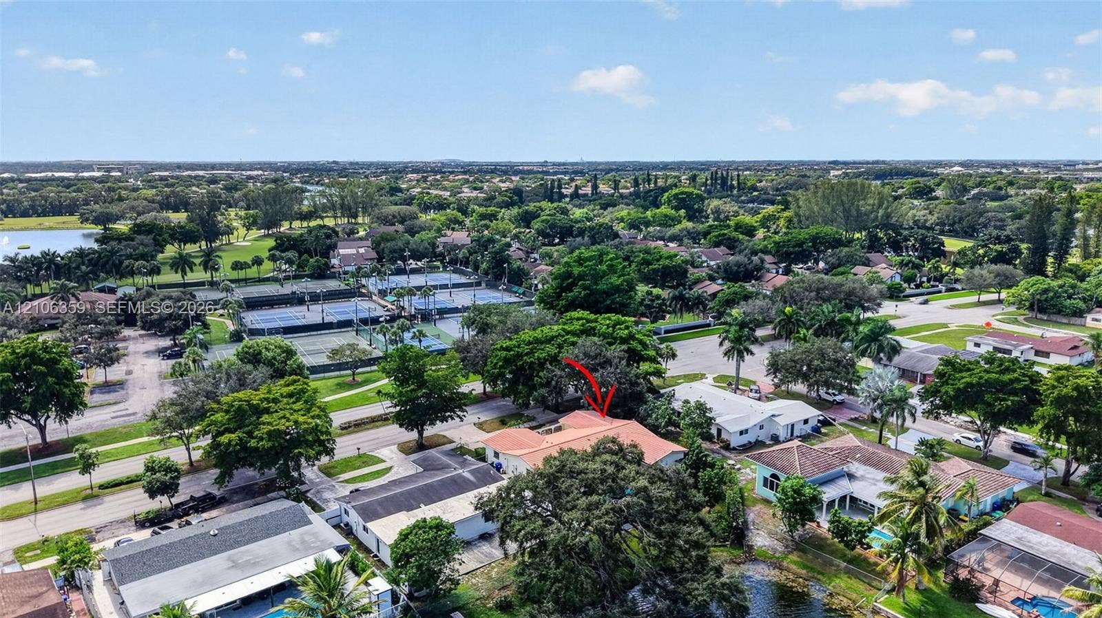 Aerial perspective featuring a single-story residence with a clay tile roof, mature trees, and proximity to neighborhood recreational courts and water features