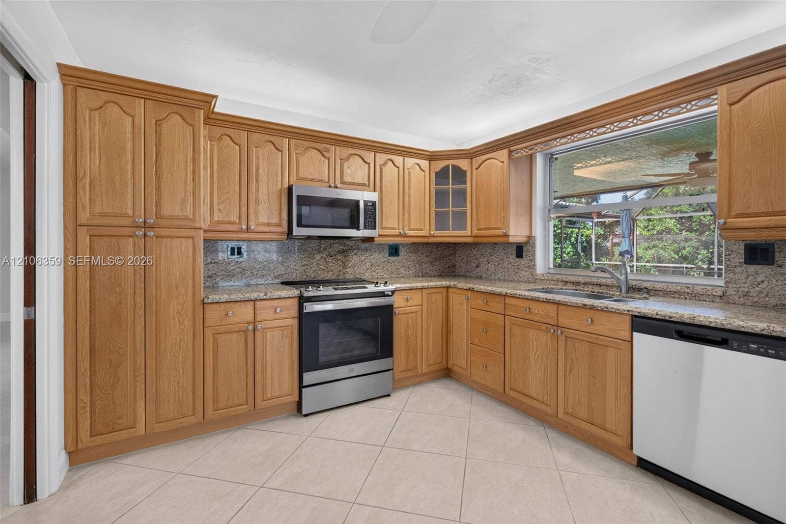 Kitchen featuring wood cabinetry, stone-finish countertops, tile flooring, and integrated stainless steel appliances