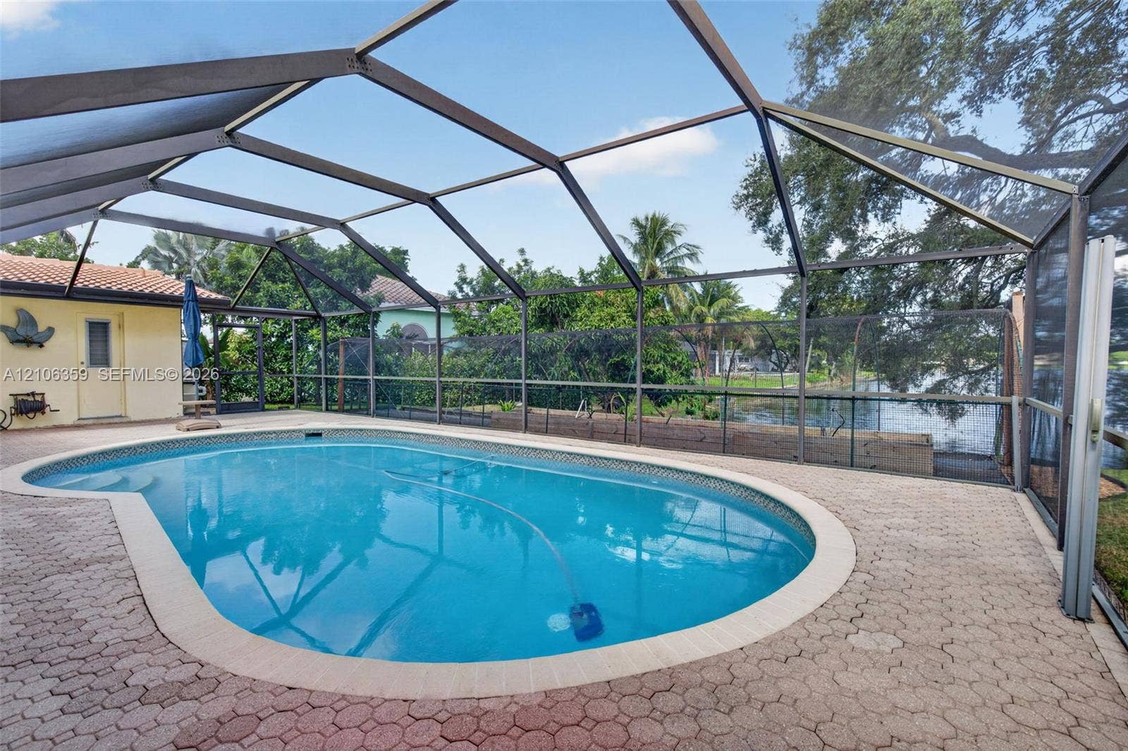 Screened-in patio area featuring a concrete paver pool deck, a kidney-shaped inground pool, and direct water frontage