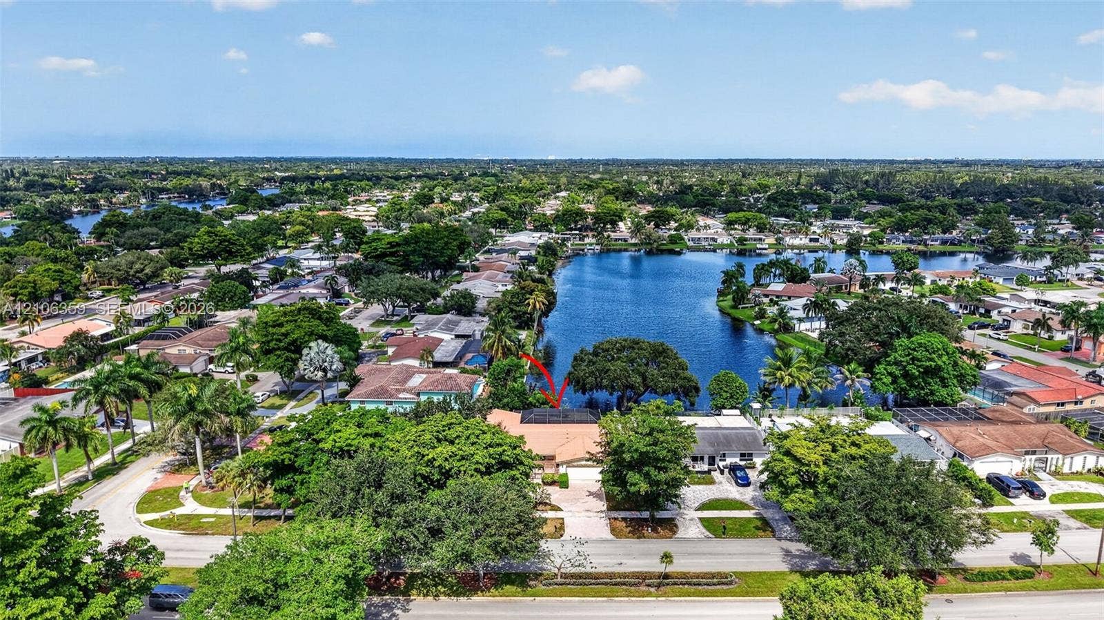 Aerial perspective of a single-story residence featuring a tile roof, paved driveway, integrated garage, and a waterfront position on a lake