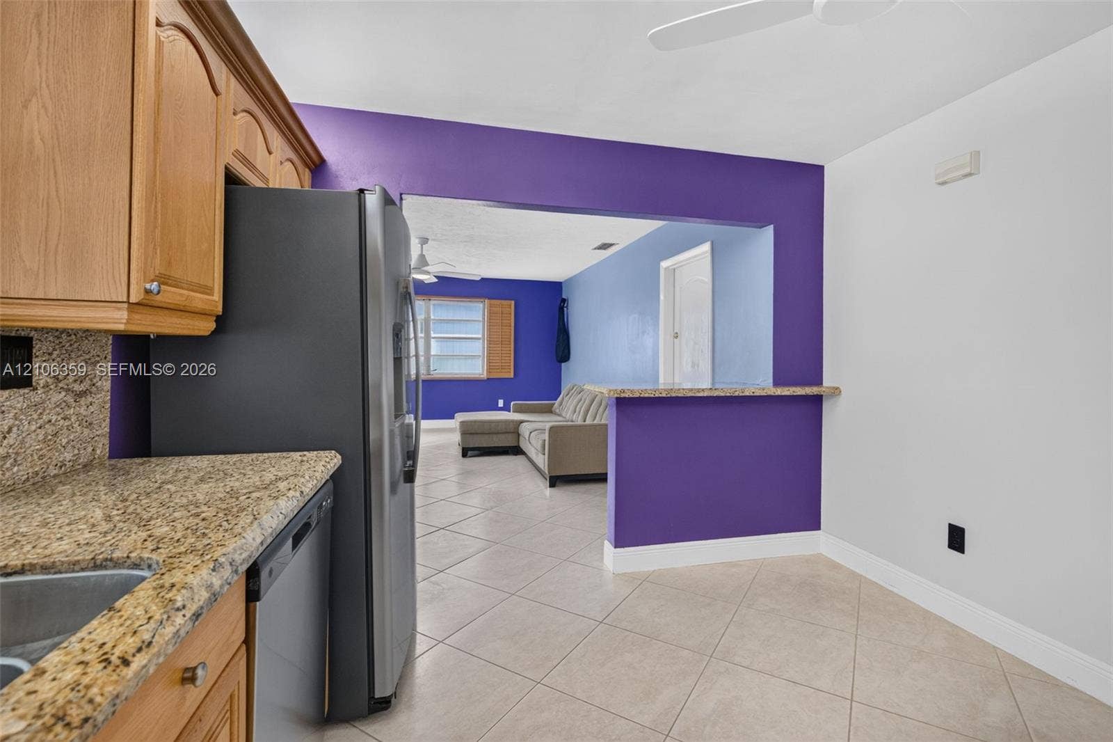 Kitchen featuring natural-finish wood cabinetry, stone-surface countertops, tile flooring, and a pass-through counter opening