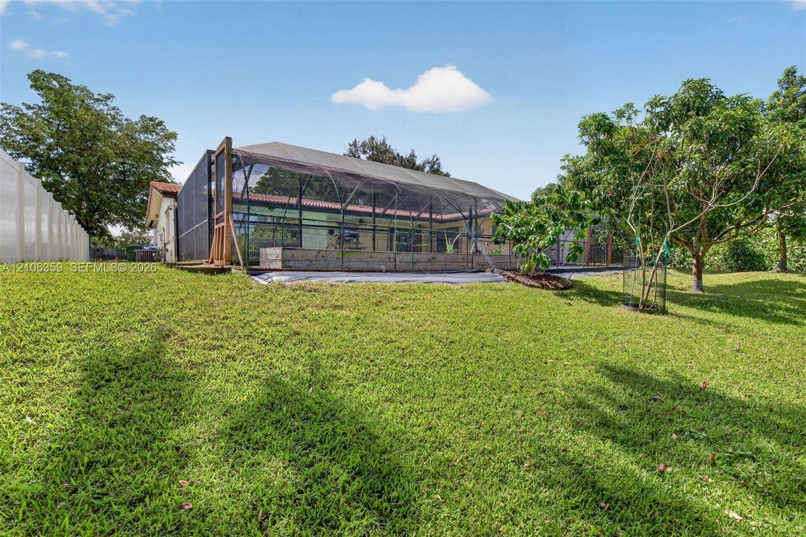 Screened-in rear patio featuring an expansive lawn, concrete retaining wall, and mature landscaping