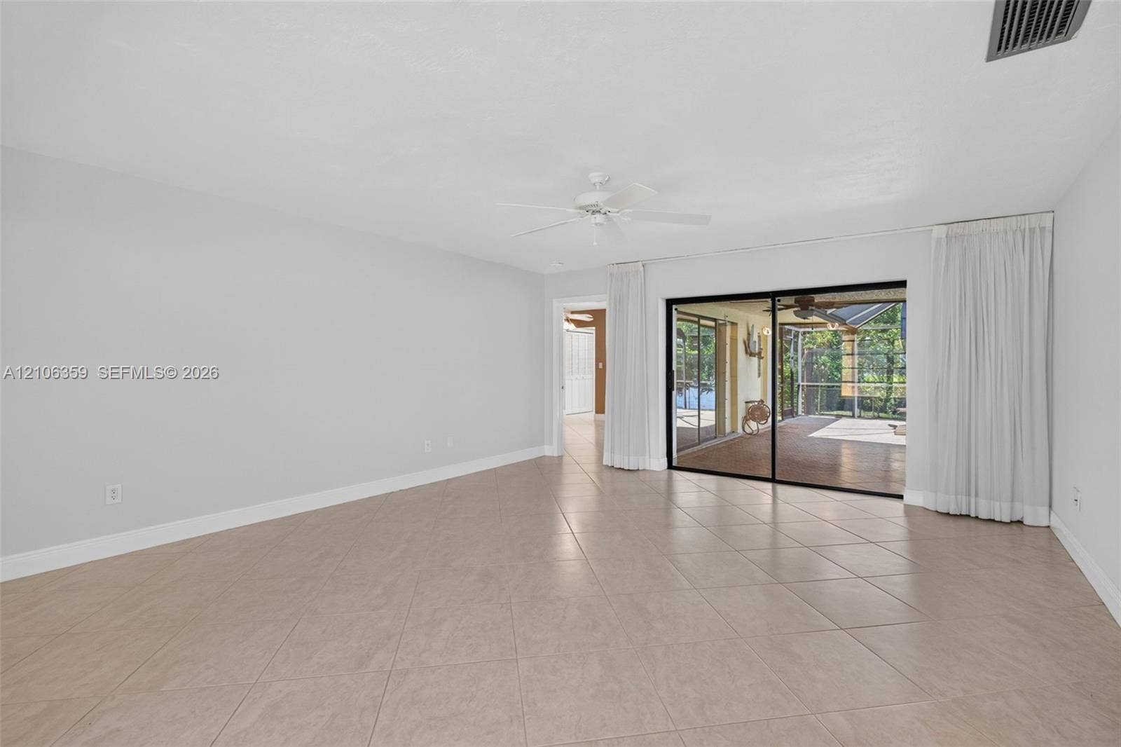 Neutral-toned interior space featuring diagonal-set tile flooring, a central ceiling fan, and sliding glass doors with direct access to a screened outdoor area