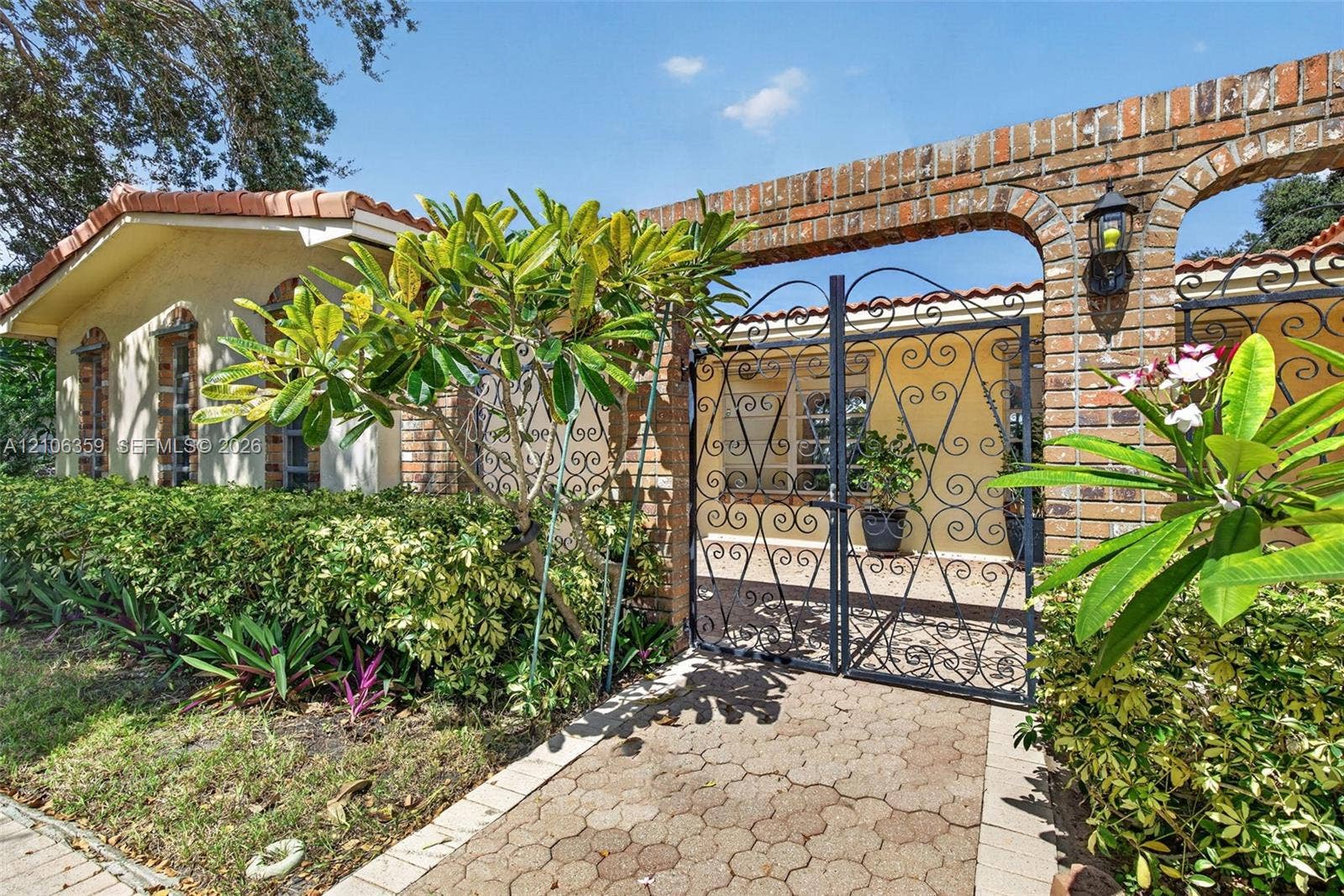 Exterior courtyard featuring a brick arched entry, custom ornamental wrought-iron gates, and a patterned stone paver walkway