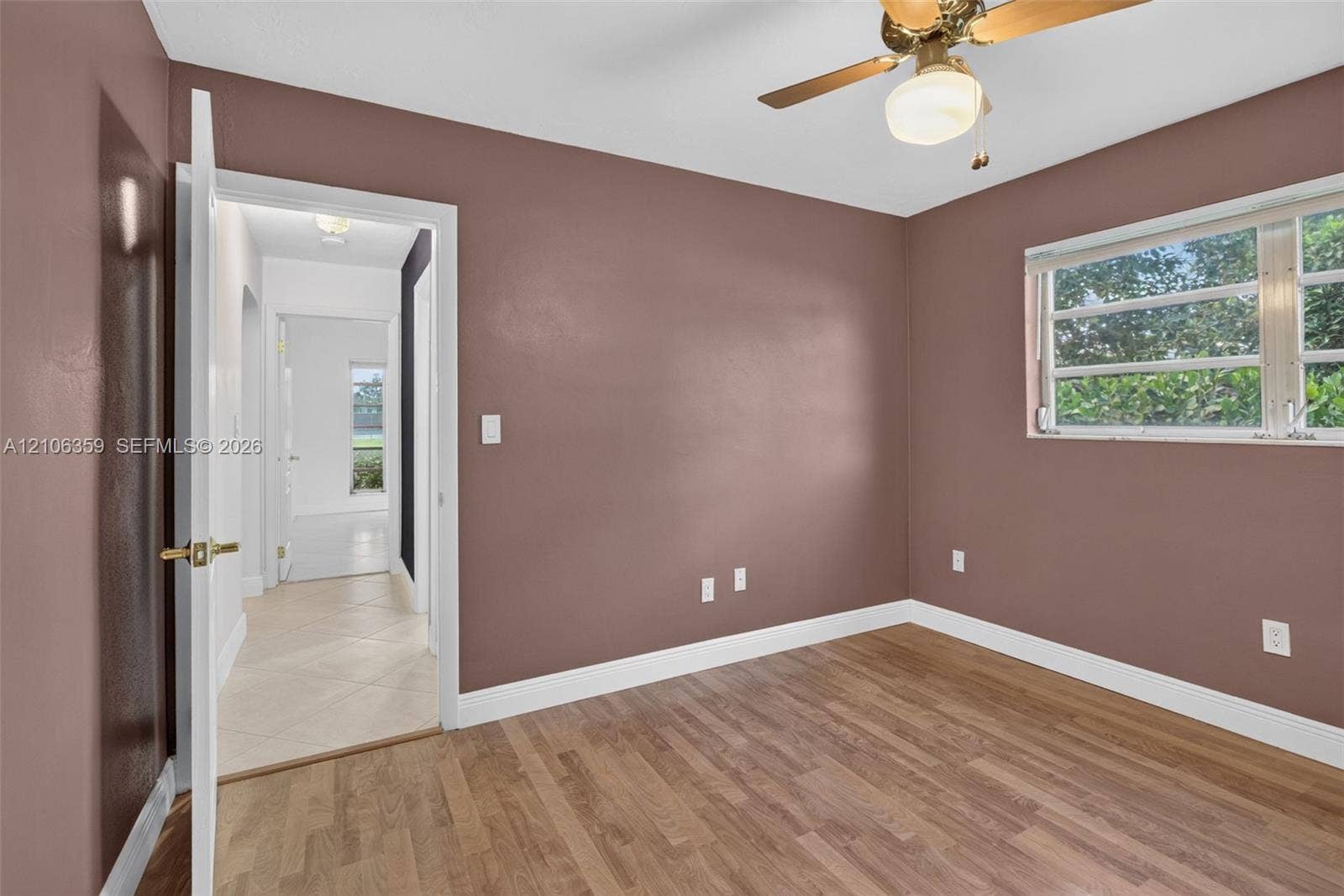 Room featuring wood-finish flooring, a horizontal sliding window, and a ceiling-mounted light fixture with fan blades