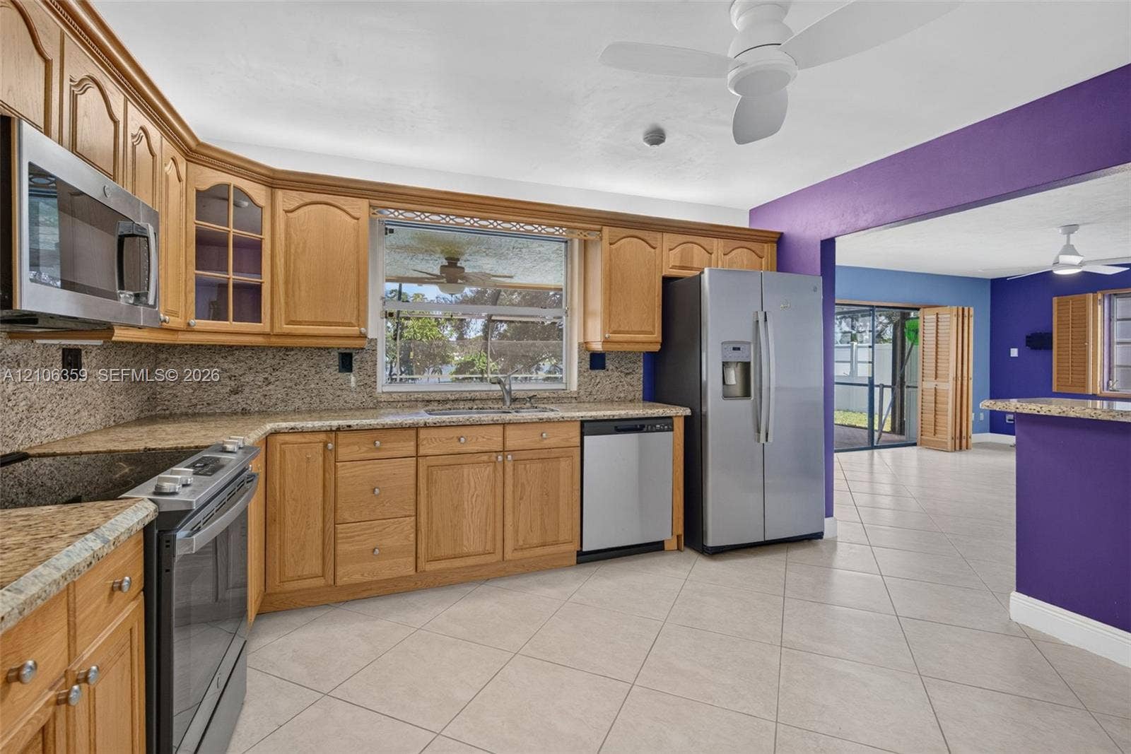Kitchen featuring natural wood cabinetry, granite countertops, stainless steel appliances, tile flooring, and a ceiling fan