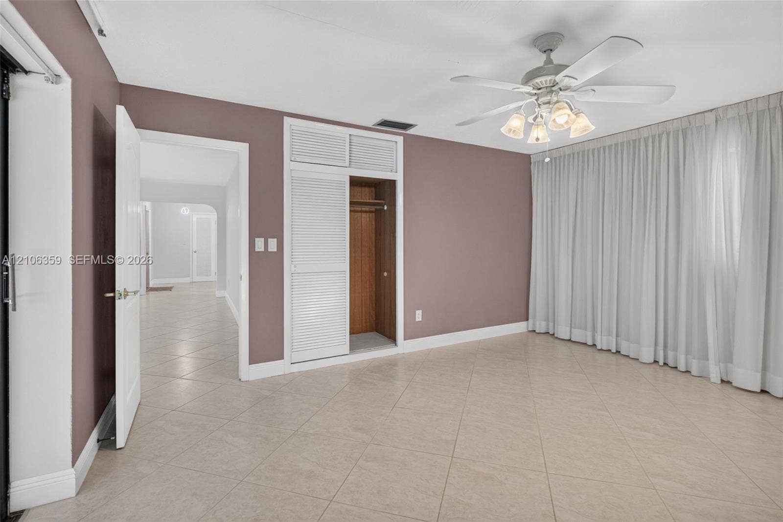 Room featuring large-format diagonal tile flooring, built-in closet with louvered doors and overhead storage, and ceiling fan with integrated light fixture