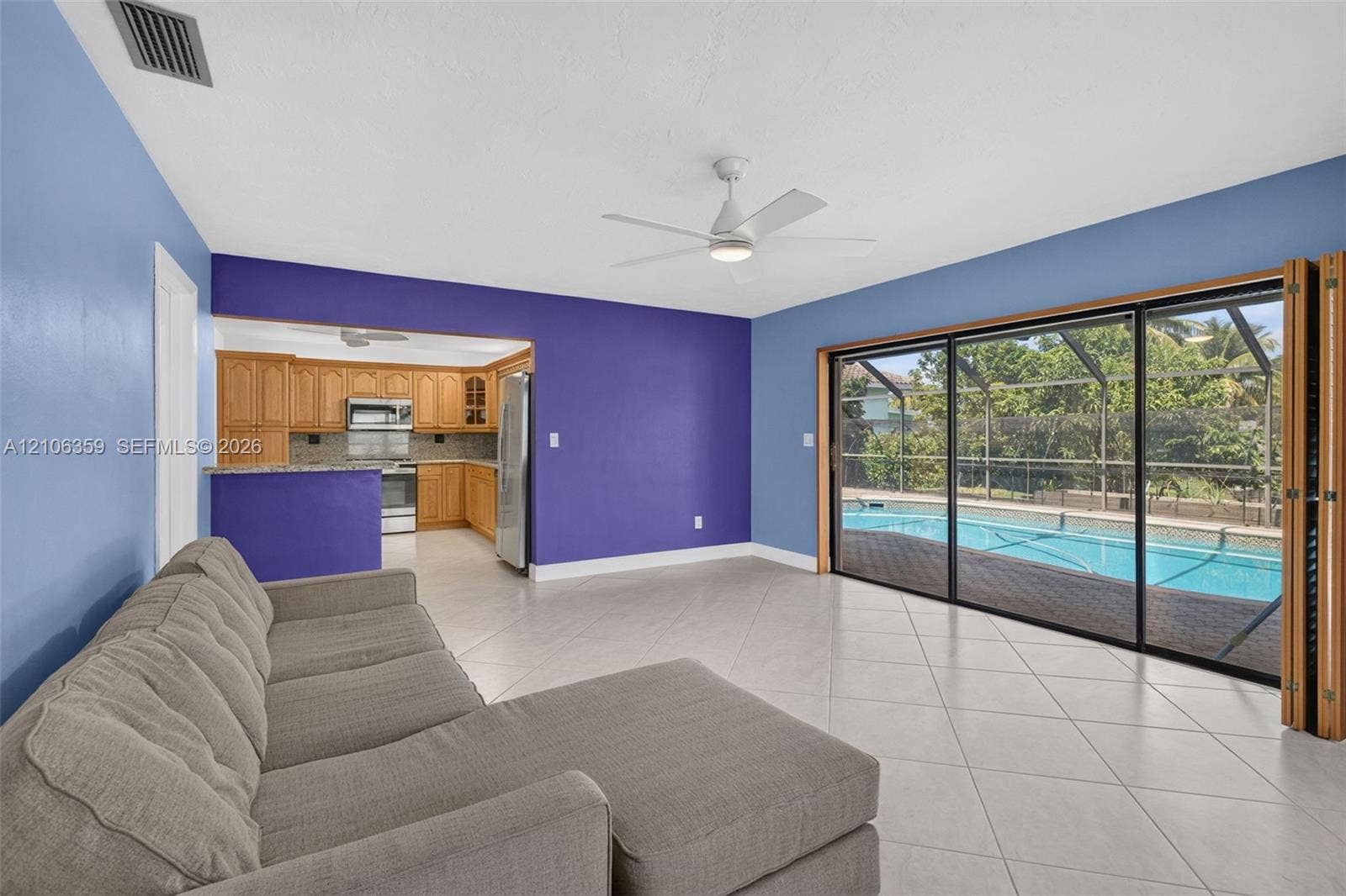 Open-concept living space featuring large-format ceramic tile flooring, a white ceiling fan, multi-panel sliding glass doors, and a screen-enclosed pool