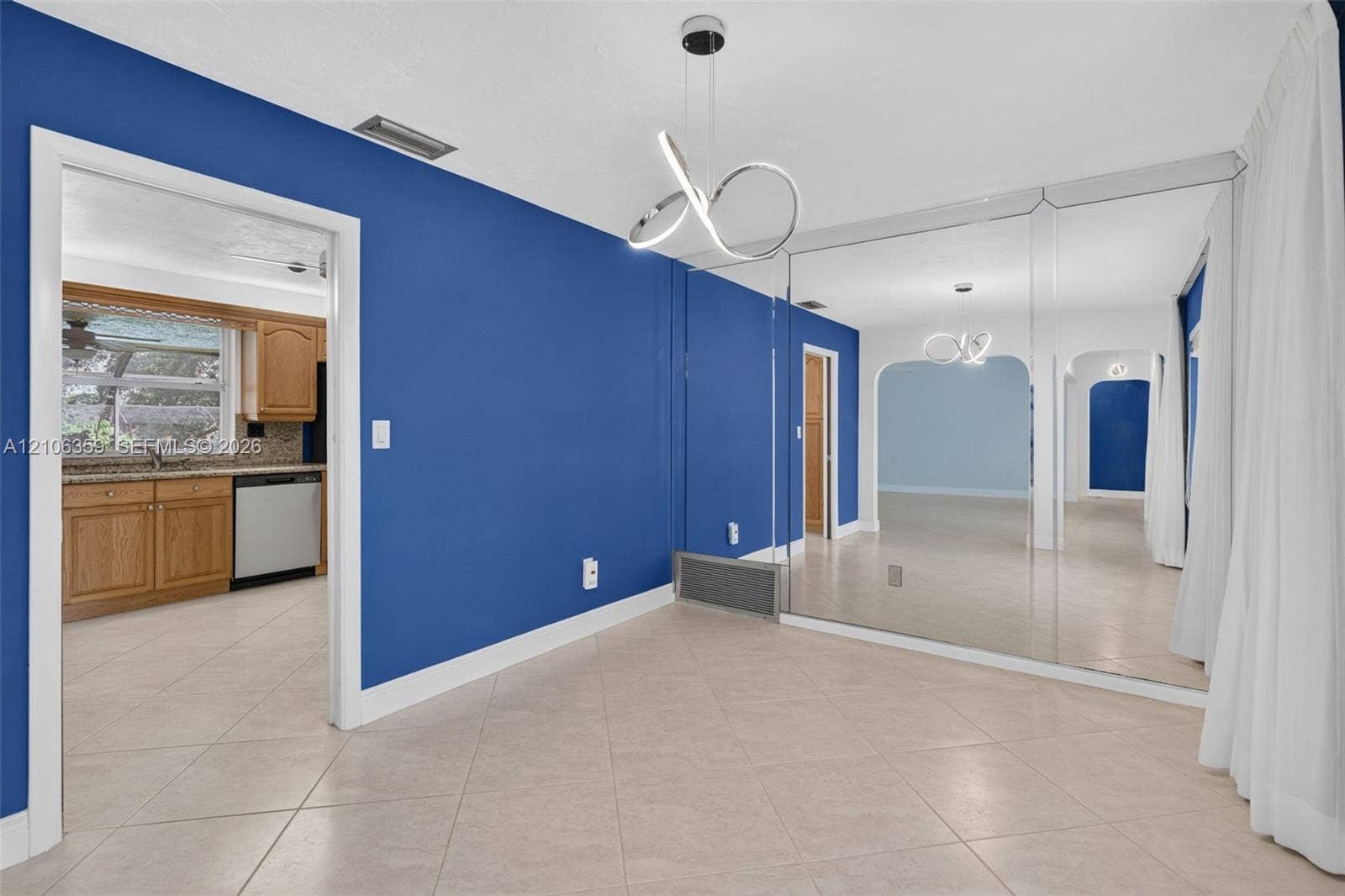 Contemporary geometric light fixture, wall-to-wall mirrored accent wall, tiled flooring, and arched doorways