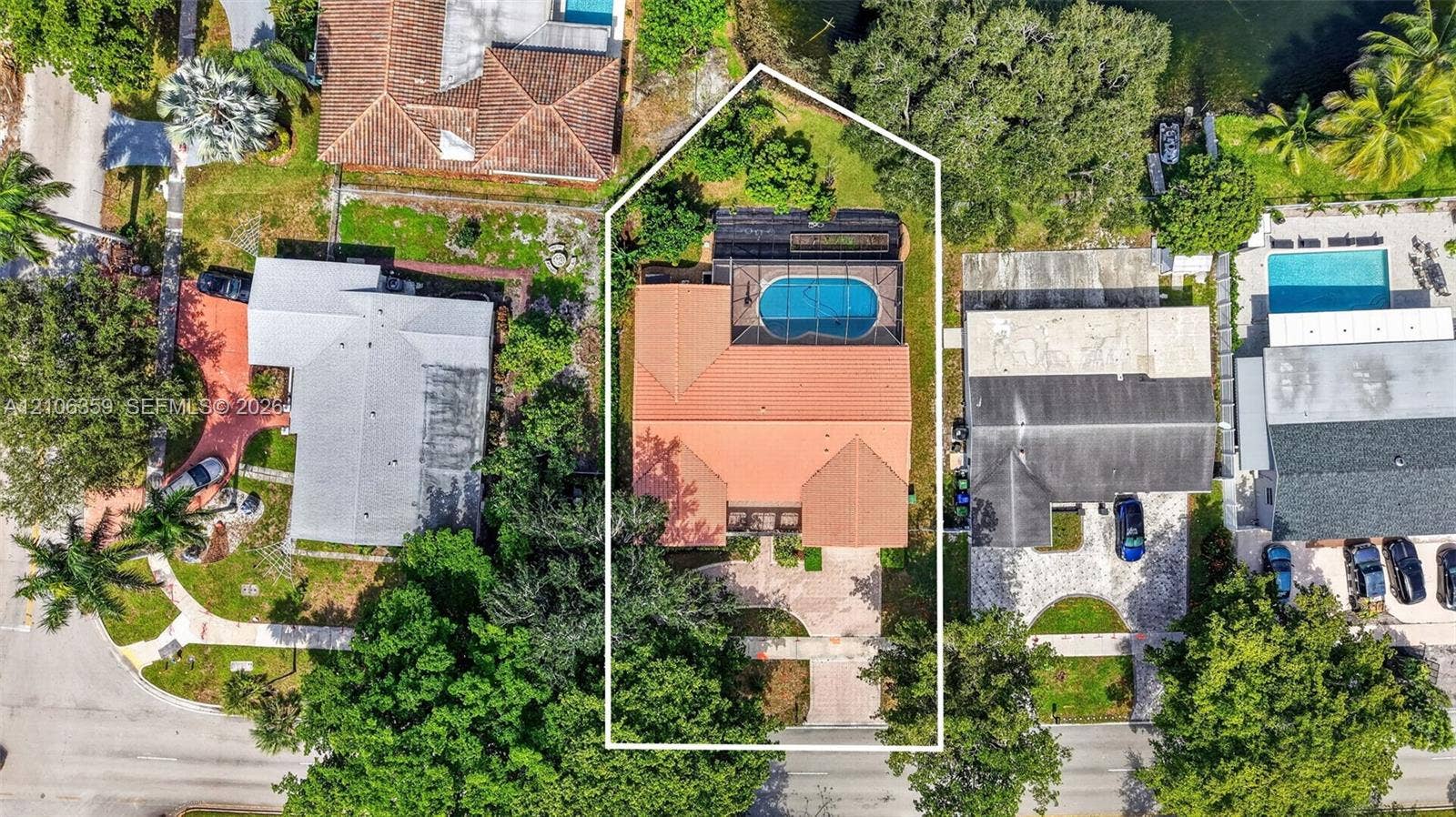 Aerial perspective featuring a tile roof, screen-enclosed pool, paver driveway, and mature landscaping