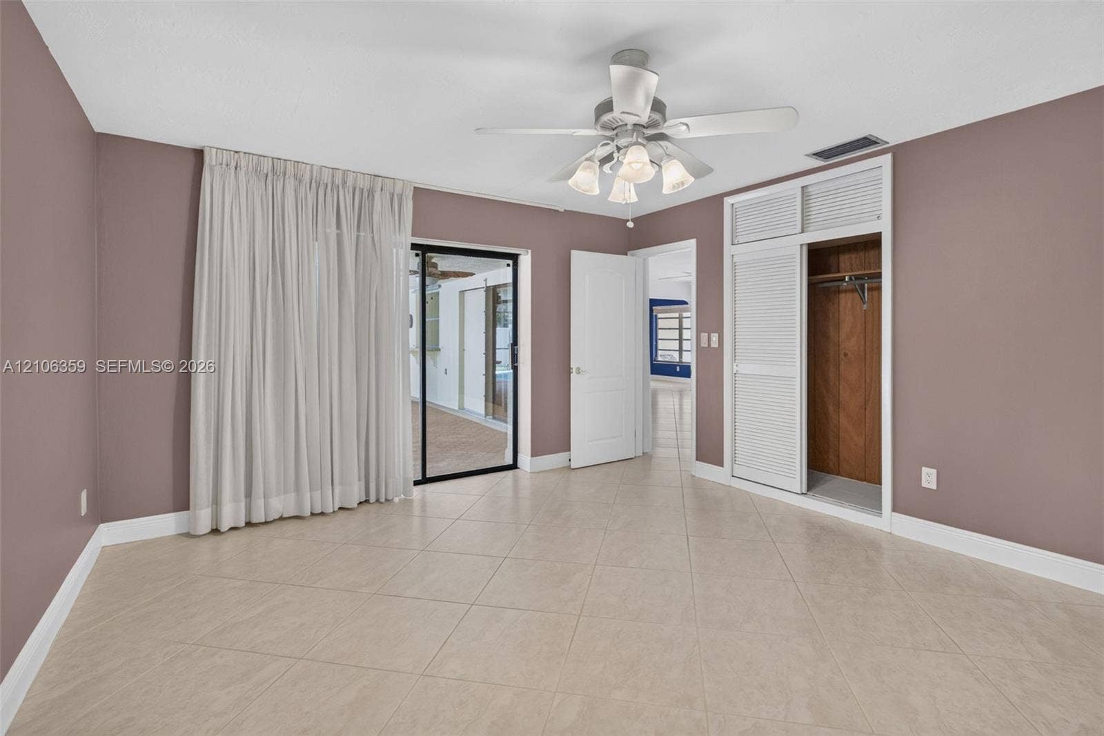 Neutral-toned tile flooring, sliding glass patio door, ceiling fan with multi-bulb light fixture, and closet with louvered doors
