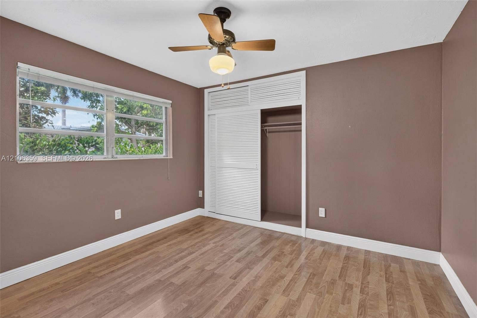 Wood-finish flooring, multi-pane window, built-in closet with louvered sliding doors, and a ceiling fan with integrated light fixture