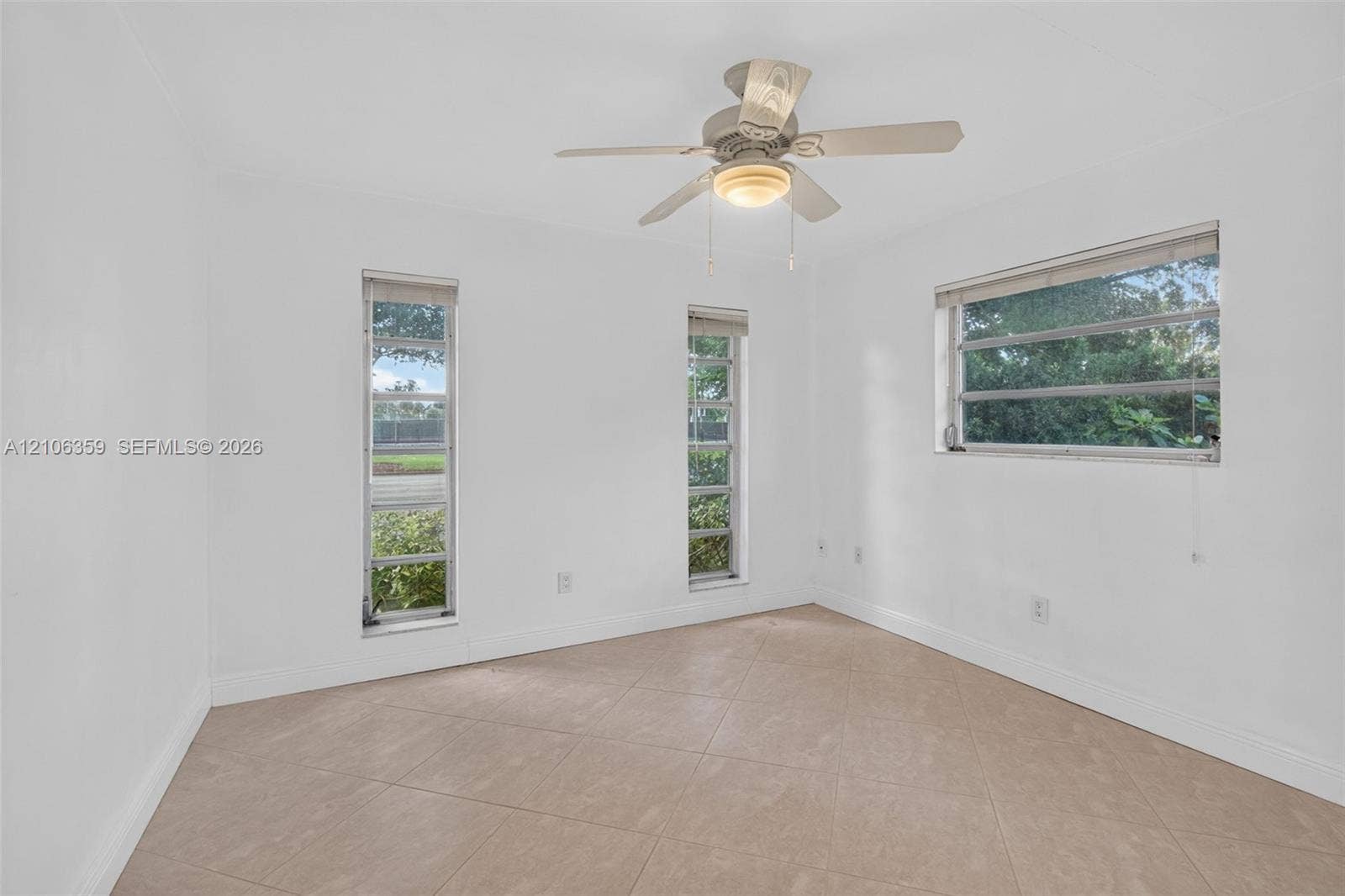 Neutral interior space featuring tile flooring, three windows with horizontal slats, and a ceiling fan with integrated lighting