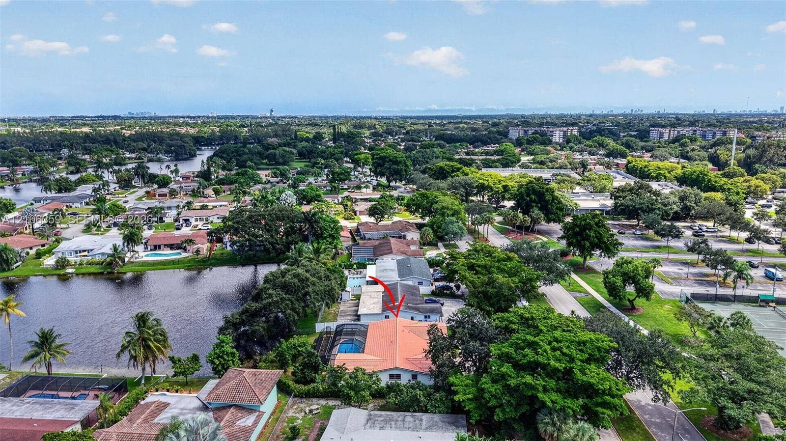 Aerial perspective featuring a single-story residence with a multi-hipped tile roof, a screened-in lanai, and a private swimming pool, situated on a waterfront lot with mature canopy trees