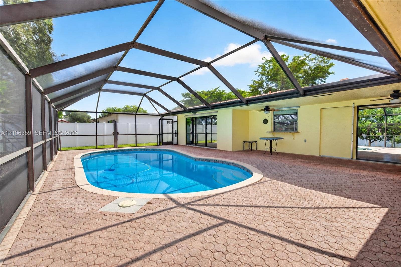 Screen-enclosed patio featuring a paver deck, in-ground swimming pool, ceiling fans, and white vinyl privacy fencing