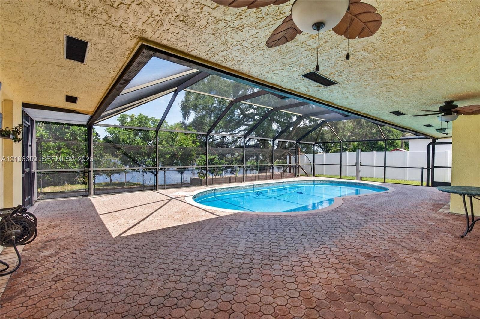 Screened lanai featuring a paved deck, built-in ceiling fans, a swimming pool, and a perimeter fence