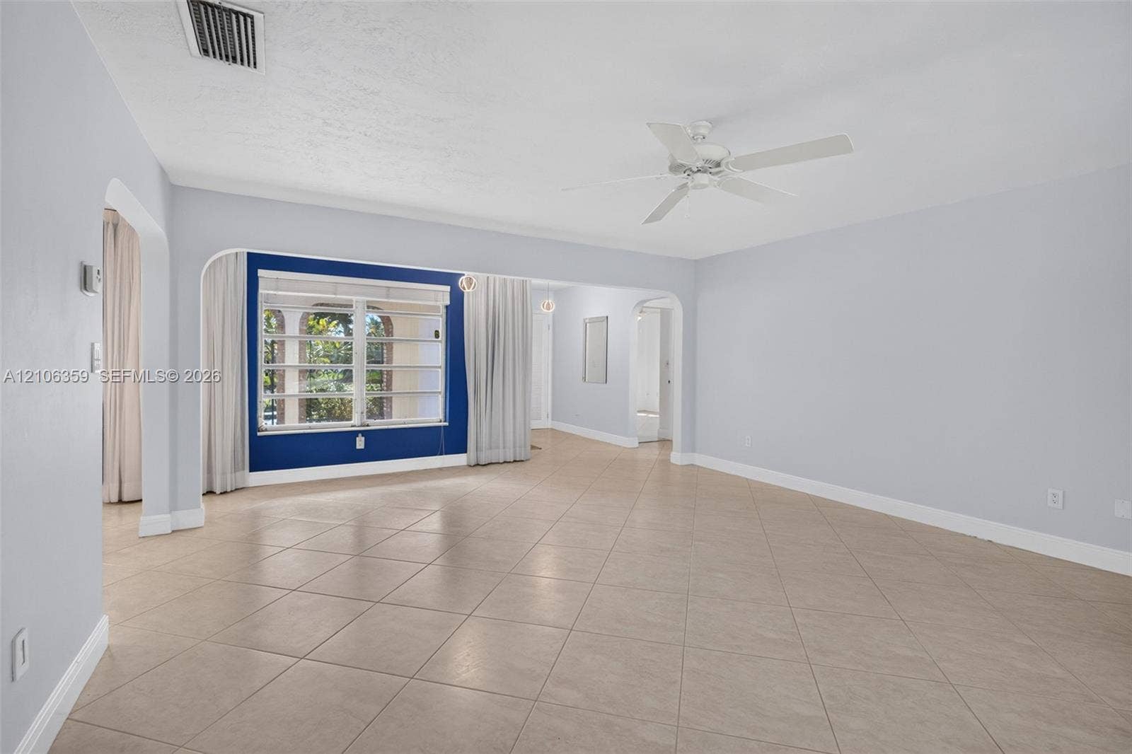 Spacious room featuring neutral ceramic tile flooring, arched entryways, a white ceiling fan, and large windows with horizontal blinds