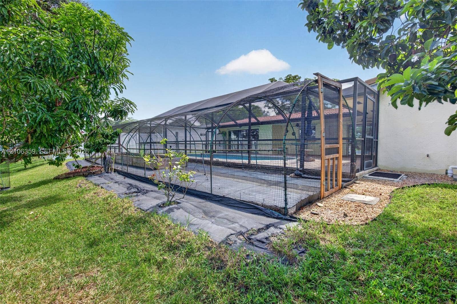 Screened-in pool enclosure featuring a concrete deck and surrounding mature landscape