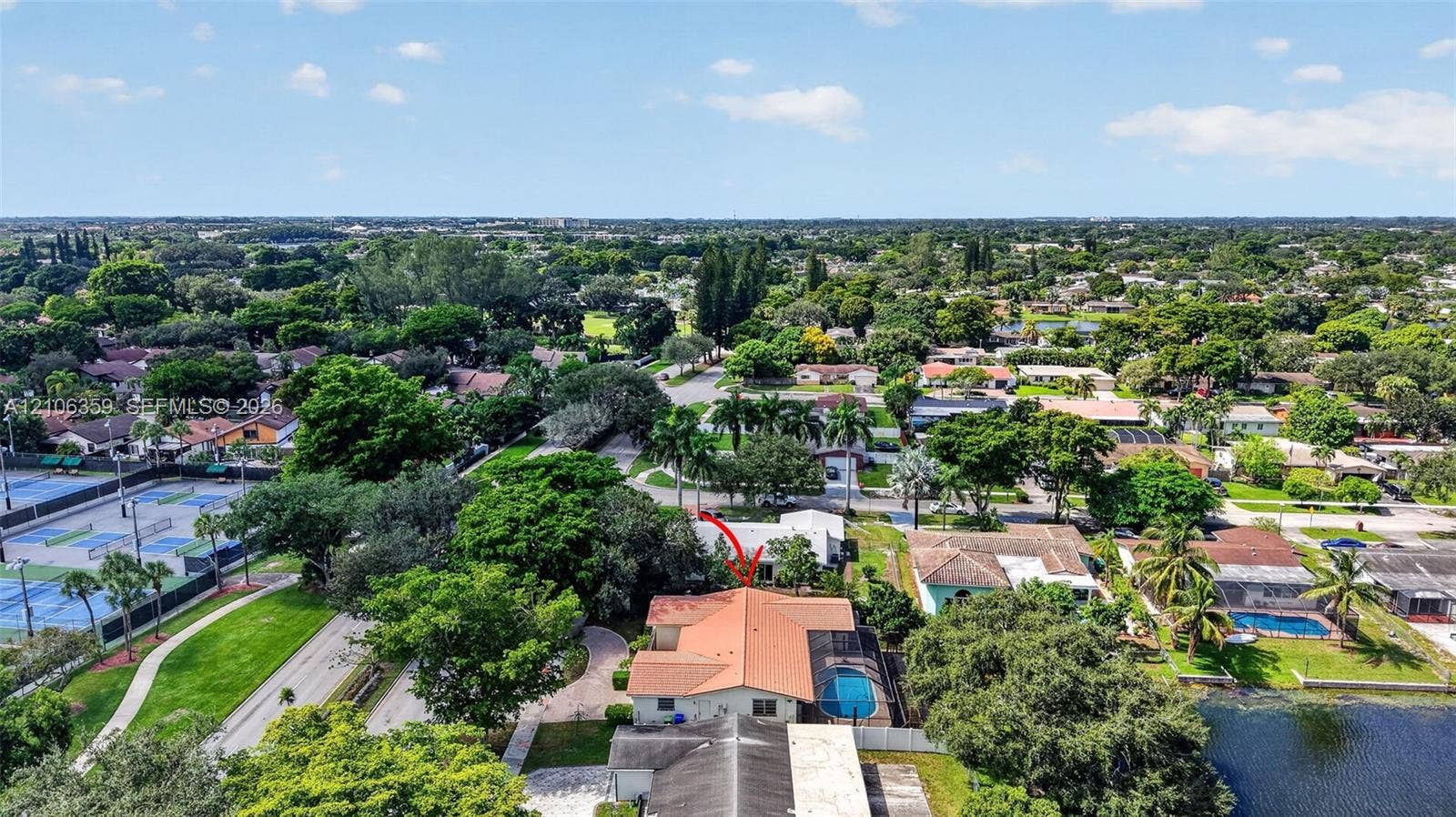 Aerial perspective of the residence featuring a terracotta-tile roof, an in-ground swimming pool with a screen enclosure, and mature perimeter landscaping
