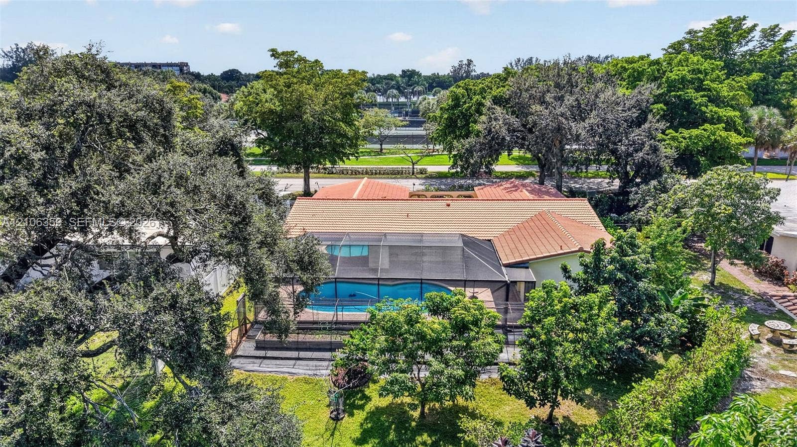Exterior aerial featuring a terracotta-tiled roof, screened-in swimming pool, and mature trees on a landscaped lot
