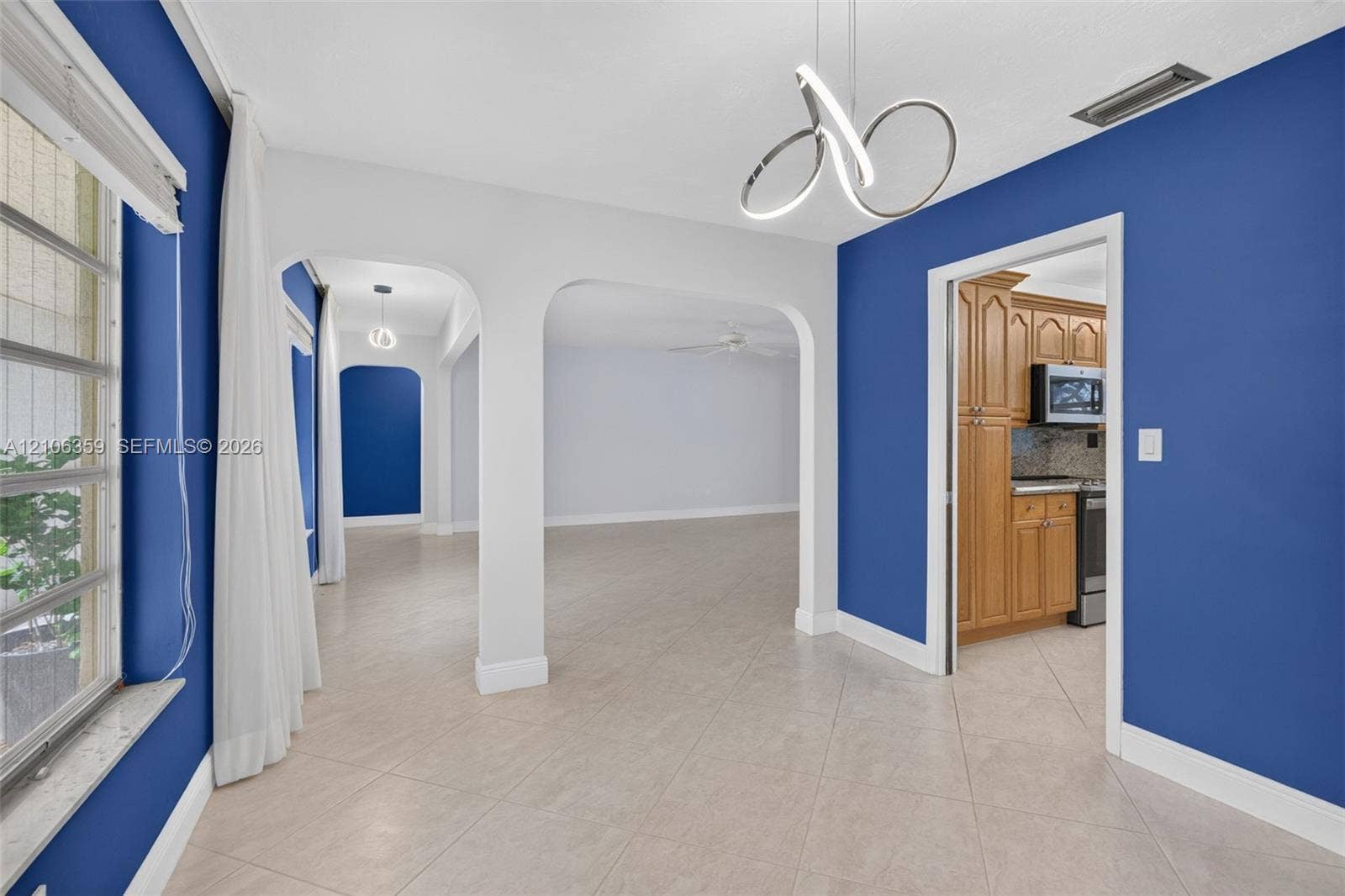Open floor plan featuring arched doorways, light-toned ceramic tile flooring, modern sculptural pendant lighting, and natural wood cabinetry