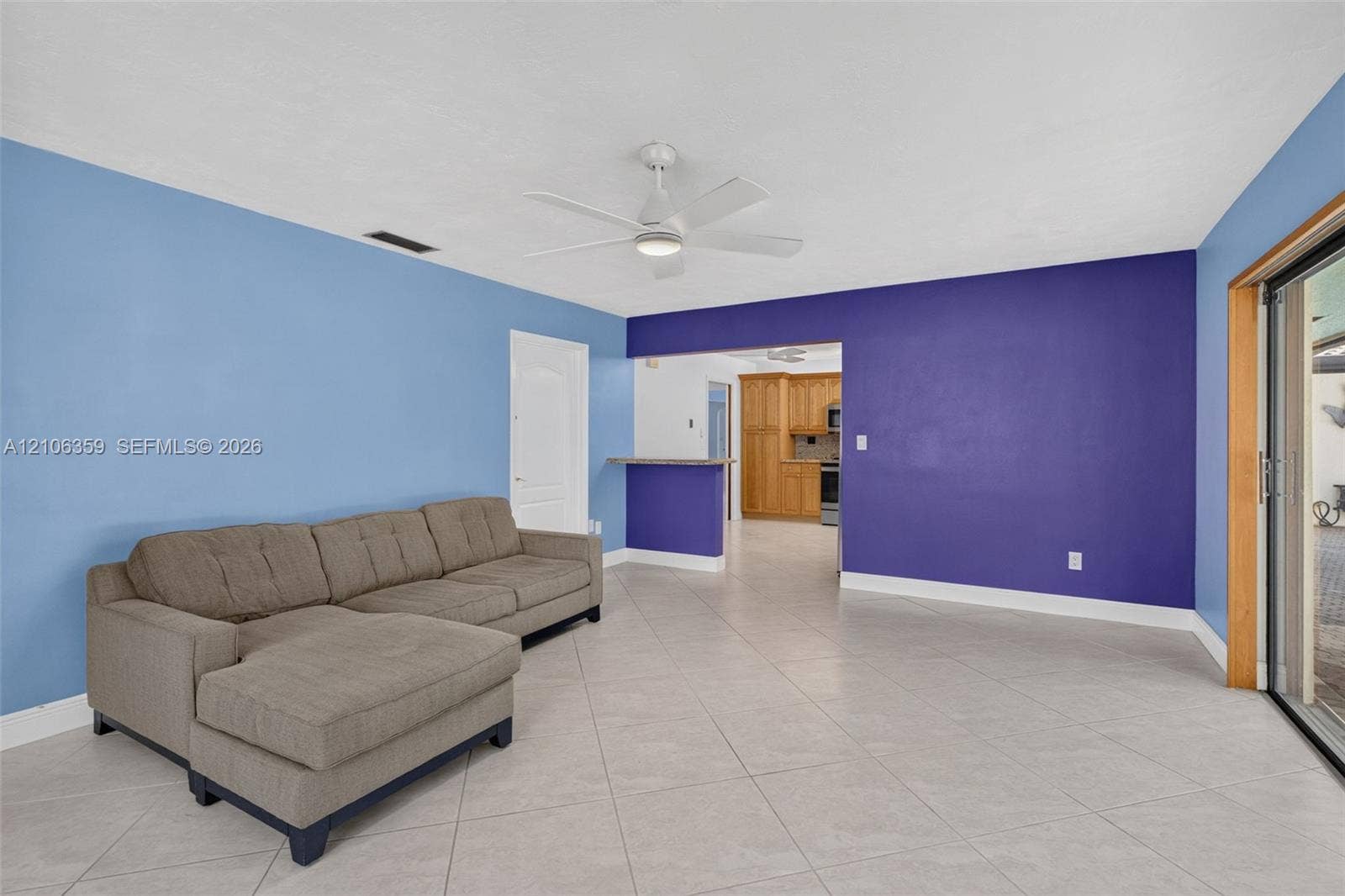 Spacious interior featuring neutral tile flooring, a ceiling fan with integrated lighting, and a built-in breakfast bar