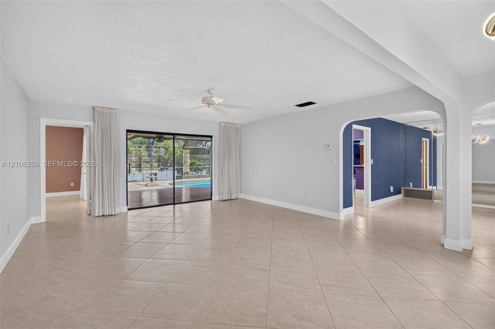 Open-concept interior featuring large-format tile flooring, arched wall openings, a ceiling fan, and sliding glass doors with exterior pool access