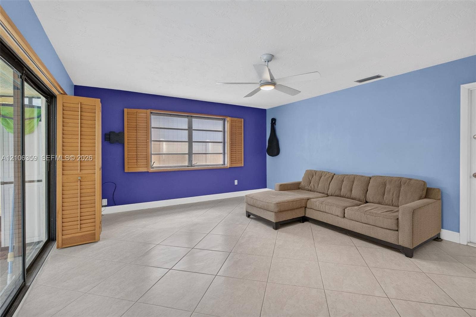 Neutral-tone ceramic tile flooring, ceiling fan with integrated lighting, and plantation-style wooden shutters framing a multi-pane window
