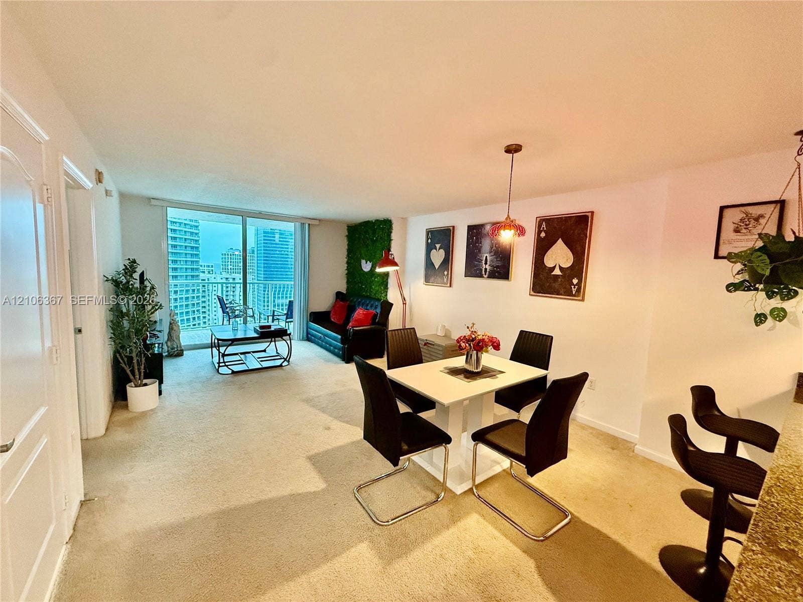 Open-concept main living area featuring floor-to-ceiling glass sliding doors, neutral carpeting, and a built-in kitchen breakfast bar