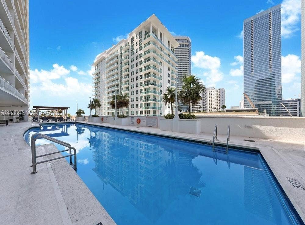 In-ground swimming pool featuring a concrete deck, metal handrails, and a surrounding perimeter wall