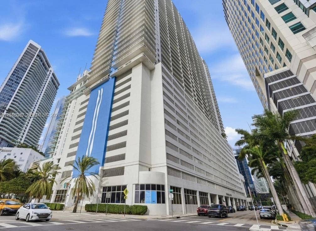 High-rise tower exterior featuring a smooth stucco faade, glass-panel balcony railings, multi-story integrated parking structure, and floor-to-ceiling windows