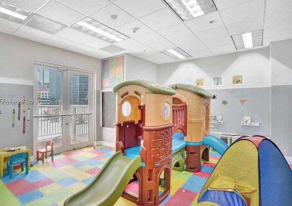 Multi-purpose room featuring drop ceiling with recessed lighting, integrated wall-mounted chalkboard, and glass-paneled double doors providing outdoor access