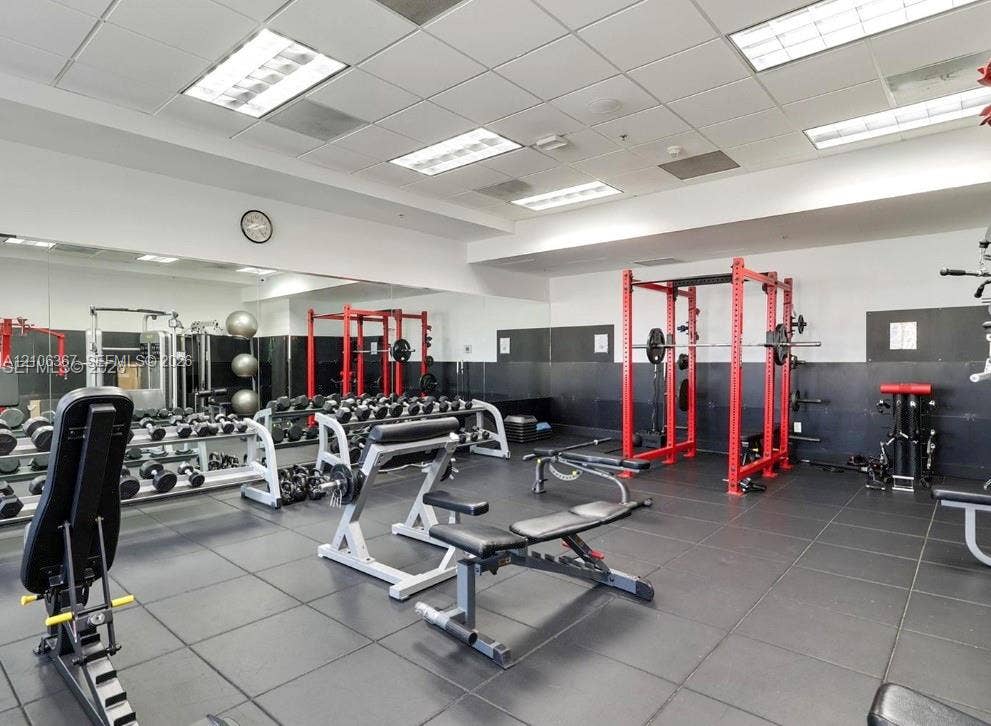 Fitness facility featuring rubberized flooring, mirrored walls, recessed grid ceiling lighting, and black wall paneling