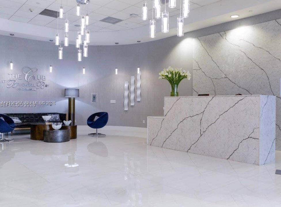 Reception area featuring a stone-faced front desk with dramatic veining, polished tile flooring, multiple cylindrical pendant light fixtures, and textured wall accents